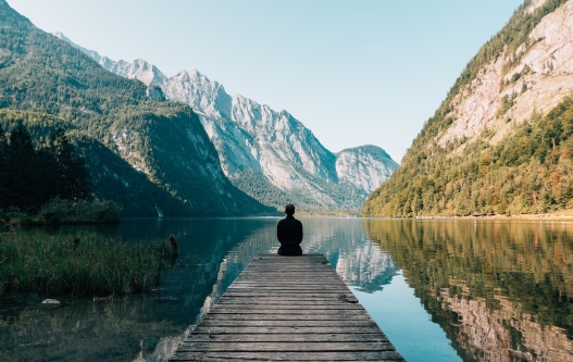Man sitting at the edge of a dock with mountains