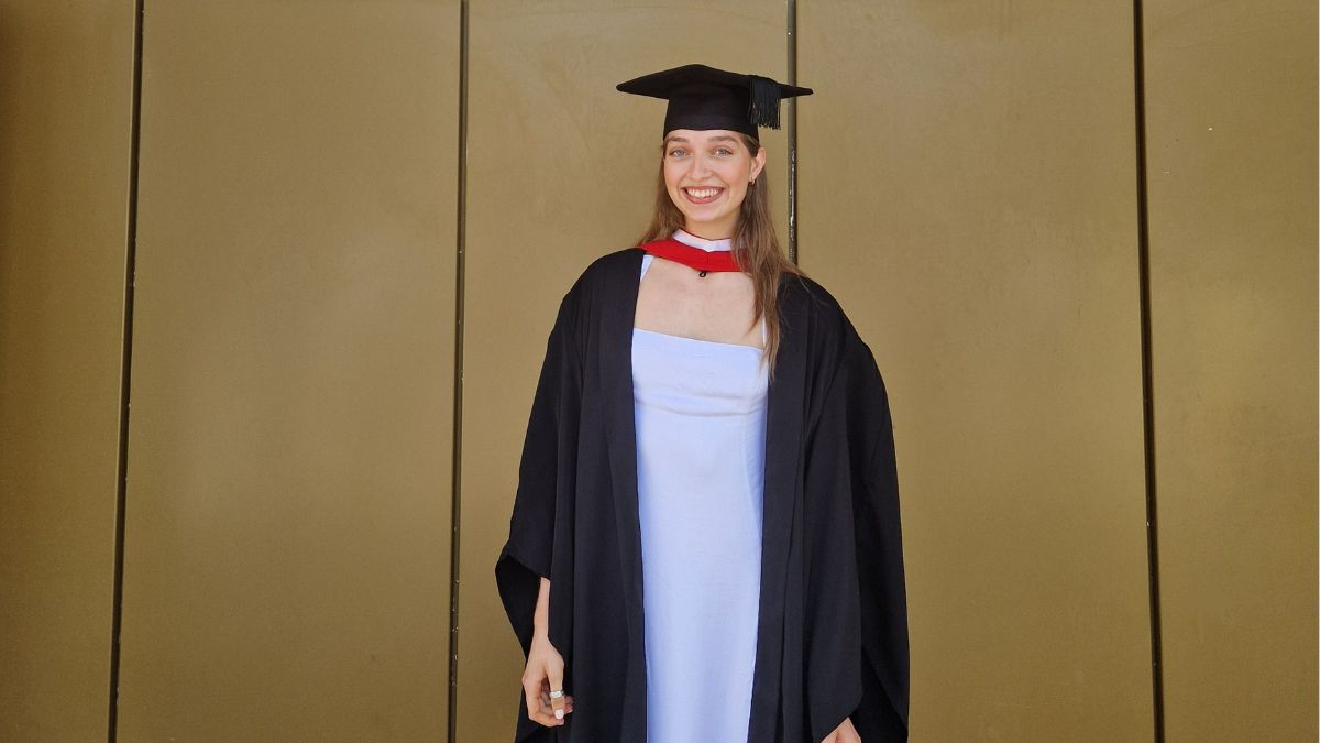 A girl wearing a black cap and gown over a white dress smile for a picture