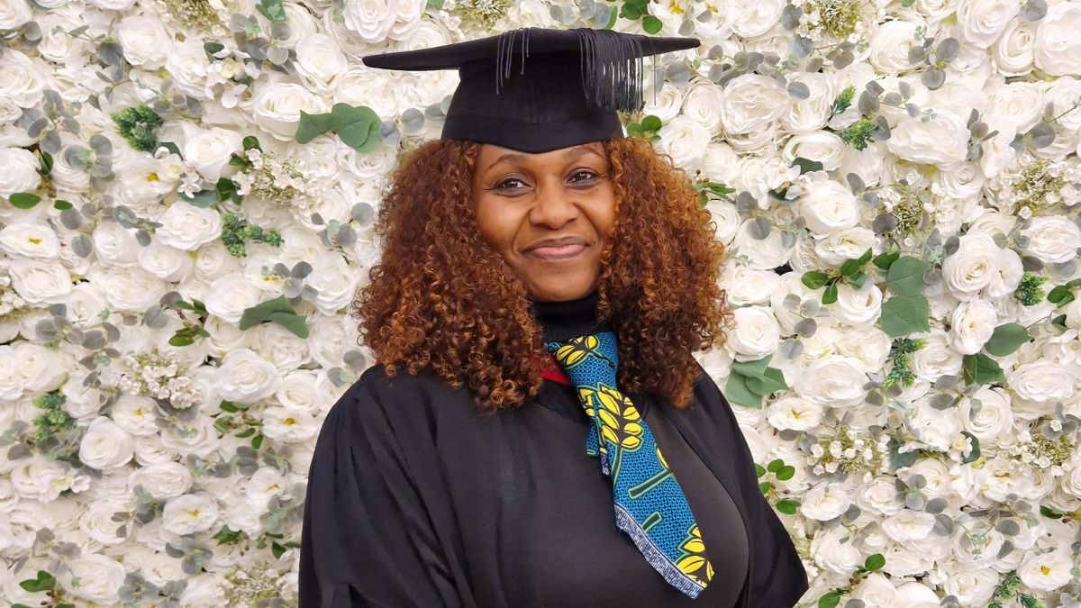 A graduate stand in front of a white flower wall