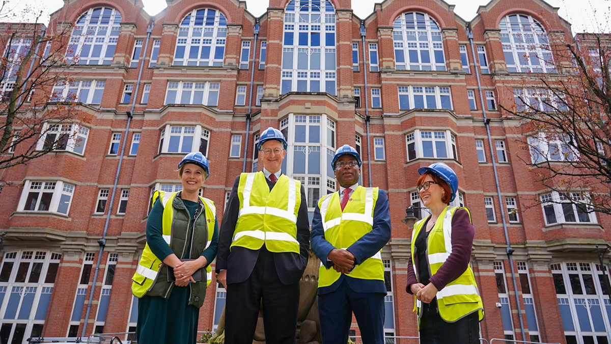 A group of four people, two women and two men, posing in front of Leeds Trinity University city campus, wearing hard hats and high-vis vests.