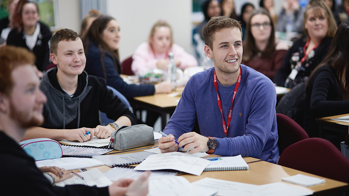 A group of students around a desk with papers and books in front of them.