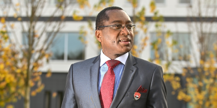 Man in glasses with grey suit jacket, blue shirt and red tie.