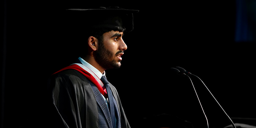 A student in graduation cap and gown giving the vote of thanks speech at Leeds Trinity University.