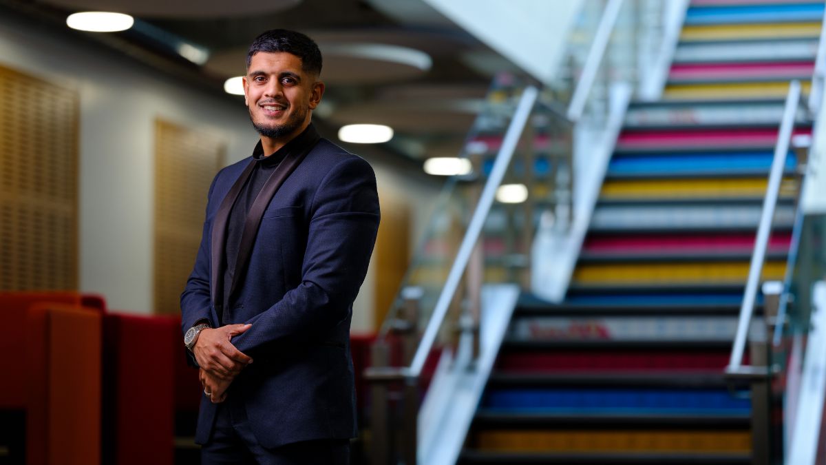 A male wearing a blue suit stands at the bottom of a multi-coloured staircase