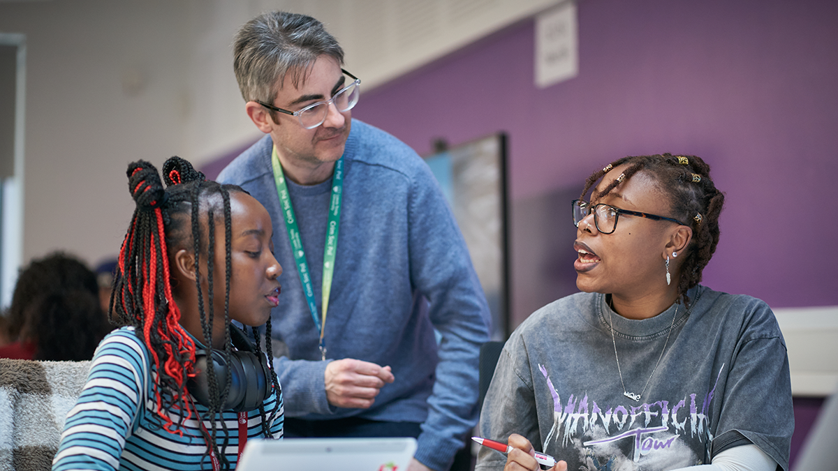 A lecturer talking to two students in a classroom at Leeds Trinity University.