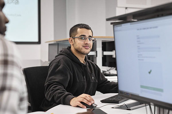 Young man in a black hoody, short hair, wearing glasses, using a computer and looking directly at the camera.